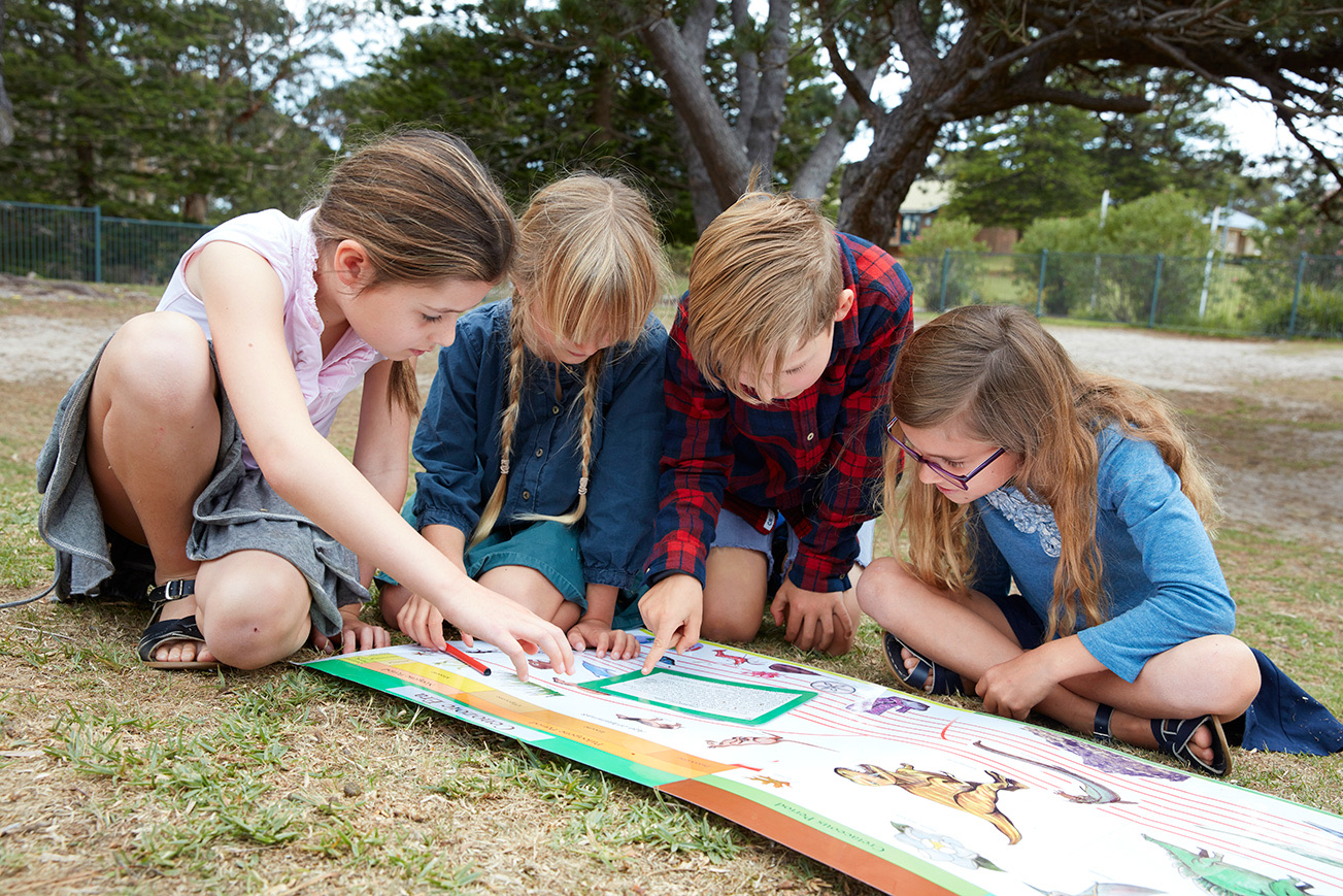 Four children working together over a chart on the grass