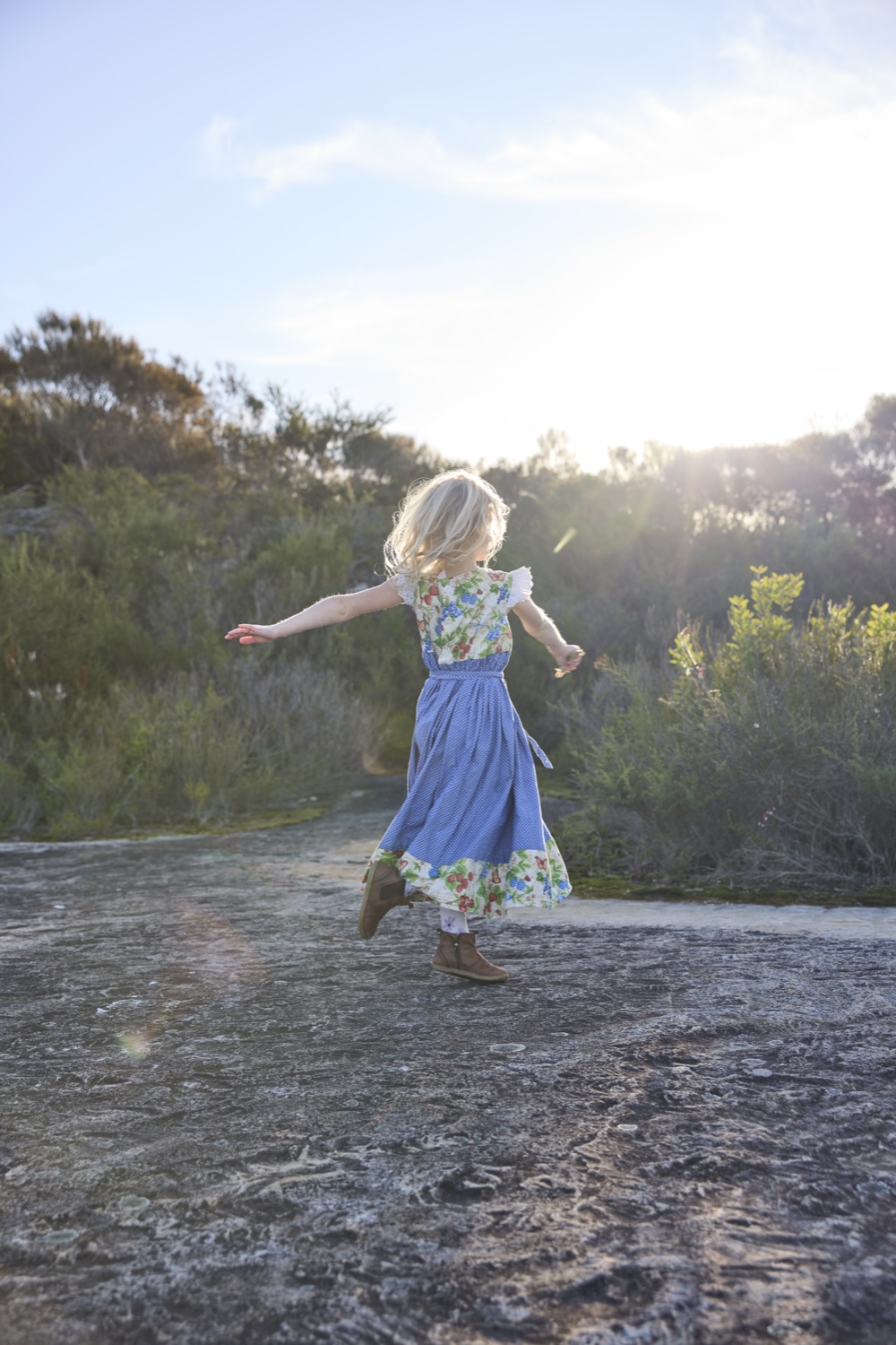A child walking across a rock platform with her arms out