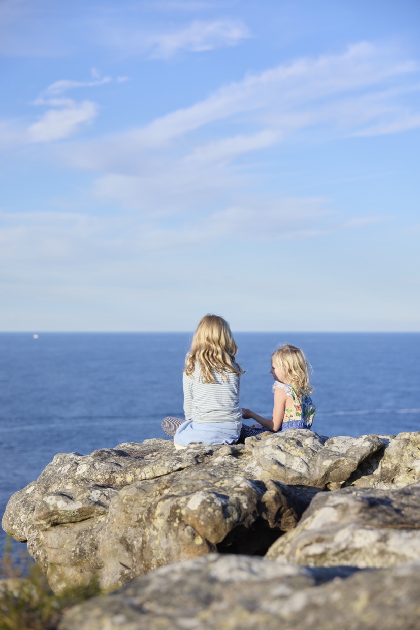 Two children sitting on a rock ledge looking out to sea
